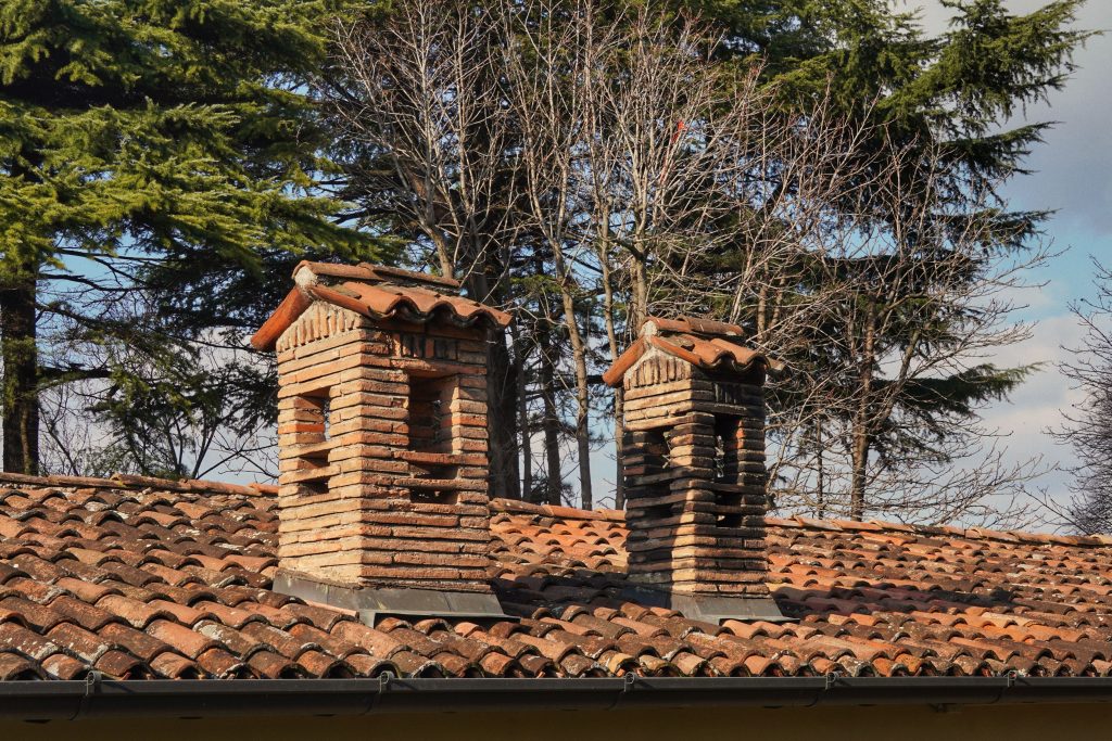 pexels photo 36027487 36027487 Two rustic brick chimneys on a red-tiled roof with a winter forest backdrop.